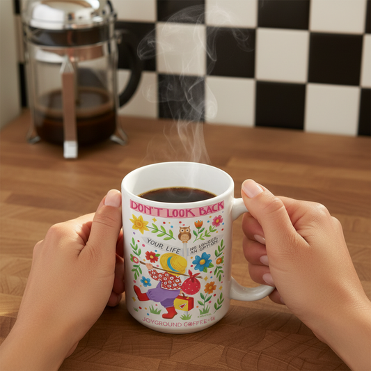 Woman holding a white Mary Engelbreit mug with colorful designs and text, steam rising from the coffee. The mug features the saying "Don't Look Back" from Joyground Coffee.