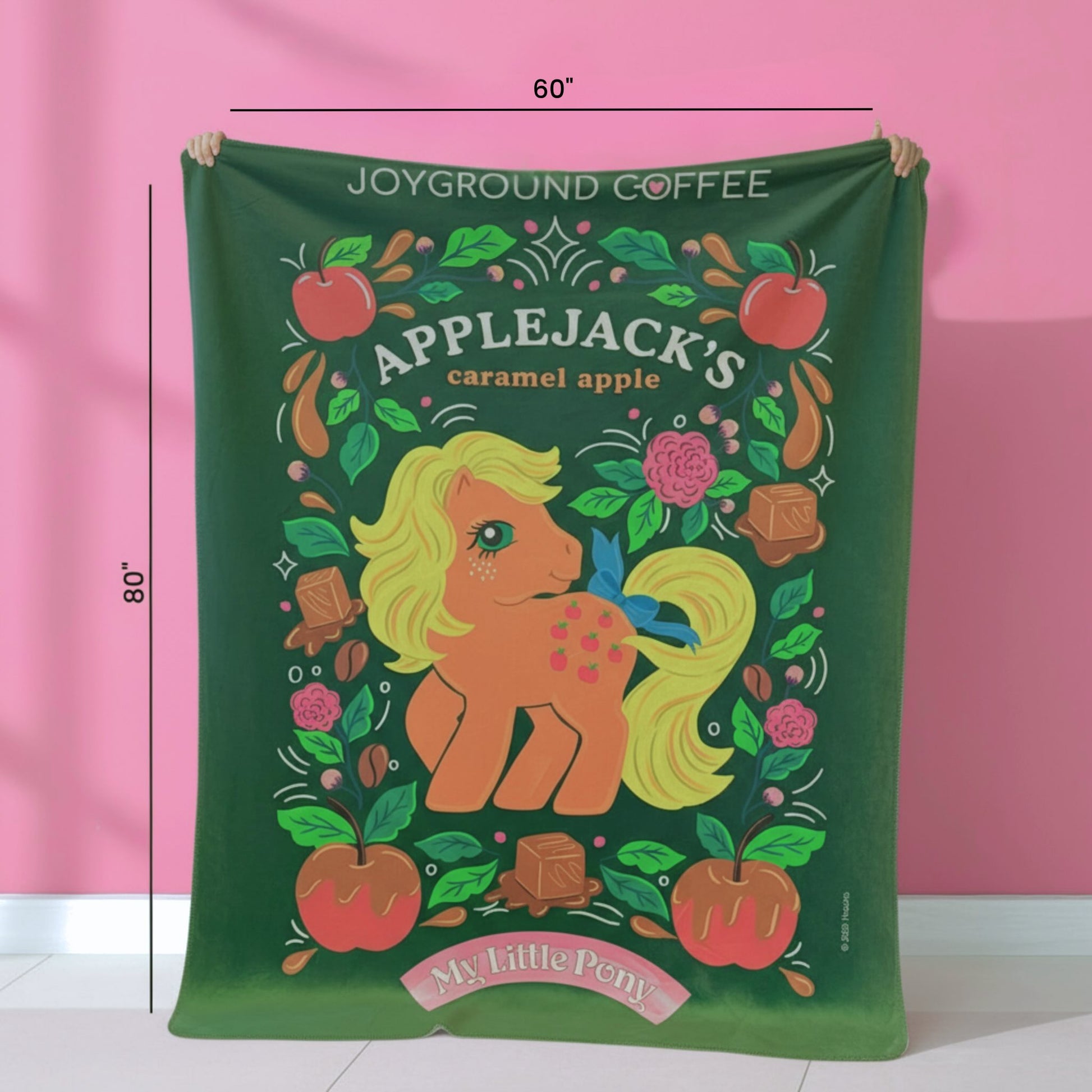 Green blanket with Applejack design from My Little Pony, held up against a pink background.