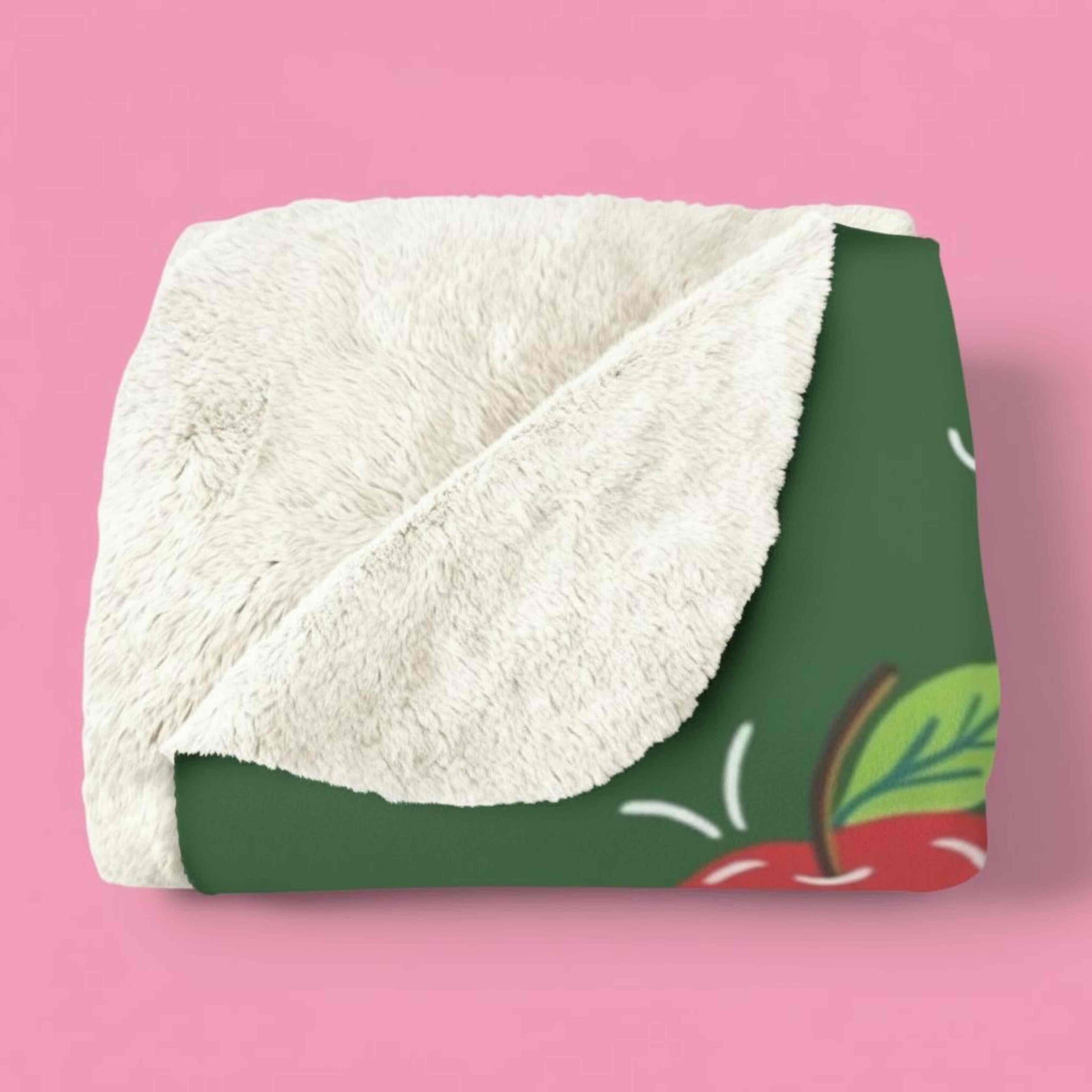Folded MLP x Joyground Coffee Applejack blanket with tan fleece on one side and green patterned design on the other, on a pink background