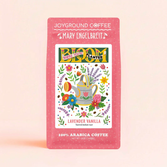 Joyground Coffee + Mary Engelbreit Bloom Where You're Planted lavender vanilla pink coffee bag featuring watering can and florals on peach background.