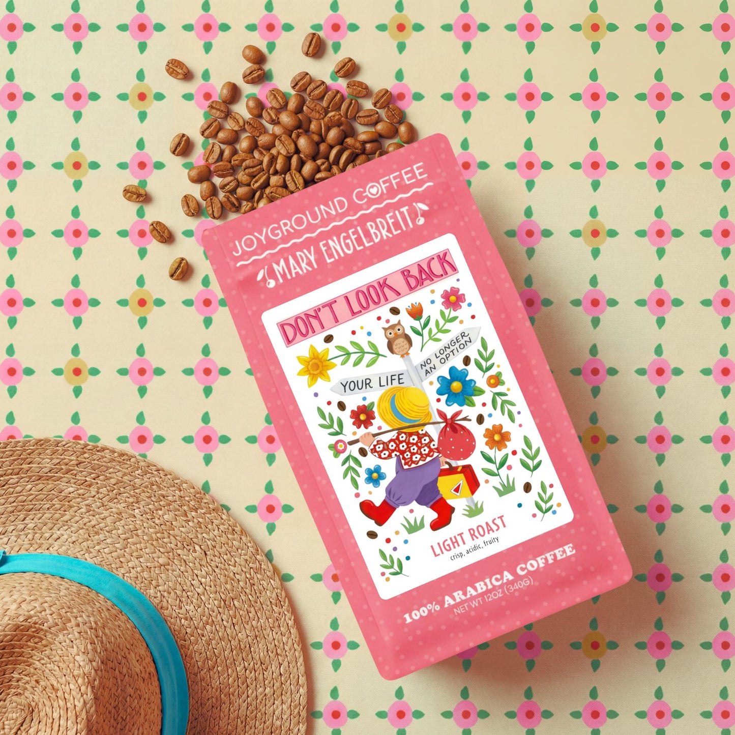 Joyground Coffee X Mary Engelbreit "Don't Look Back" package with coffee beans and a straw hat on a floral patterned background
