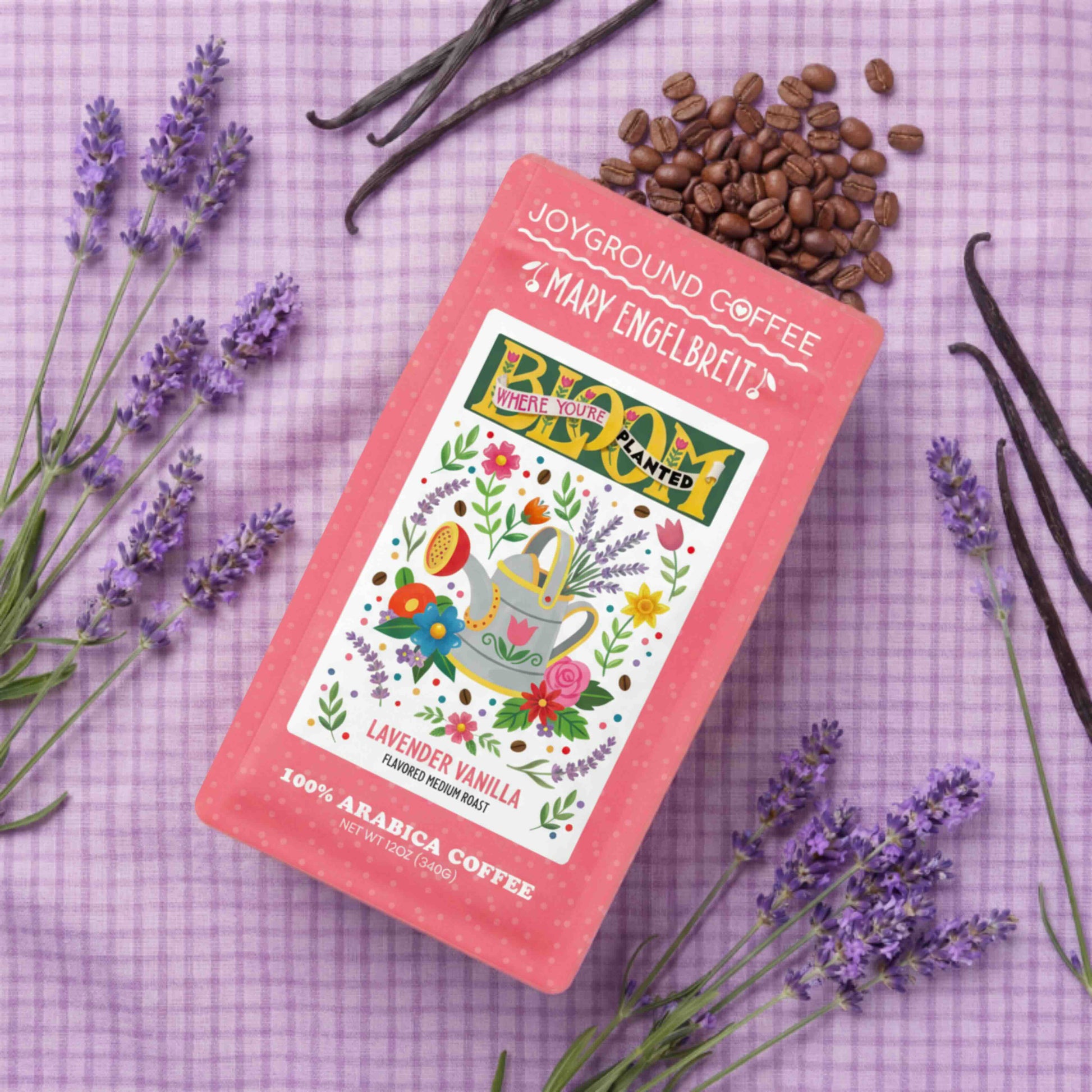 Joyground Coffee x Mary Engelbreit Bloom Where You're Planted package with lavender, vanilla beans, and coffee beans on a purple checkered background