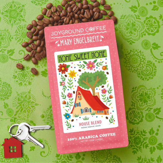 Joyground Coffee + Mary Engelbreit Home Sweet Home house blend coffee medium roast packaging with coffee beans and keys on a green patterned background