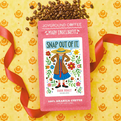 Joyground Coffee package with 'Mary Engelbreit' Snap Out of It design on a yellow background with coffee beans and ribbons.