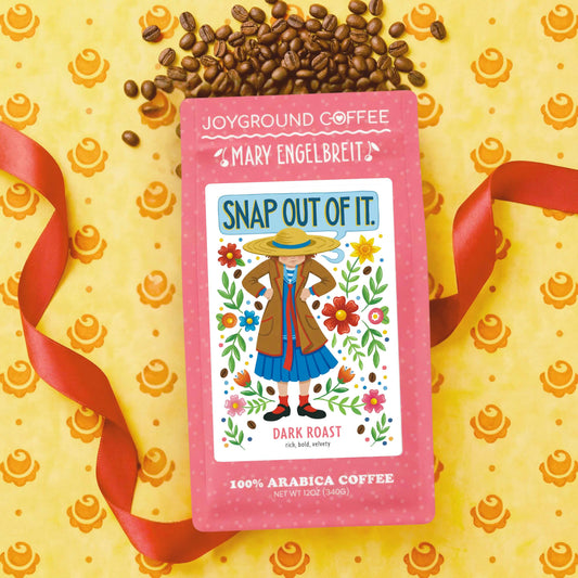 Joyground Coffee package with 'Mary Engelbreit' Snap Out of It design on a yellow background with coffee beans and ribbons.