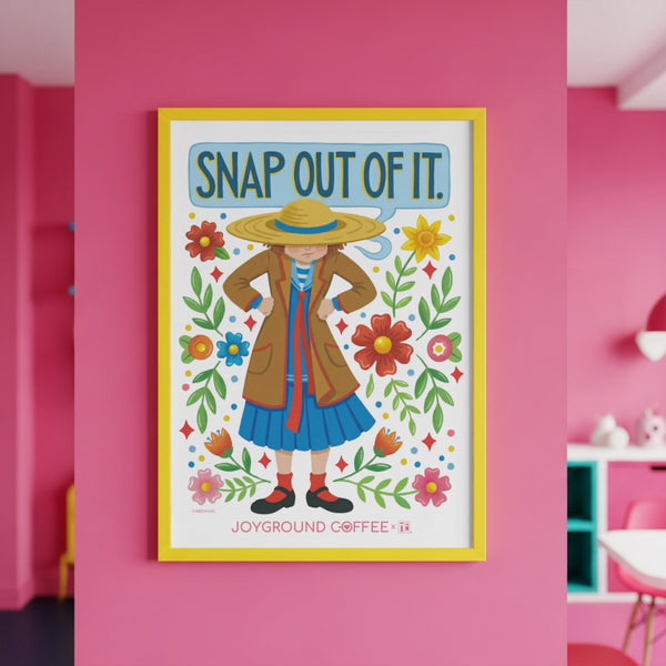 Framed artwork with a Mary Engelbreit character and floral design on a pink wall, featuring the text Snap Out of It and Joyground Coffee.