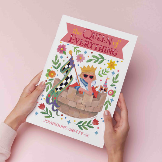 Mary Engelbreit art print titled 'The Queen of Everything' by Joyground Coffee on a pink background held by 2 hands