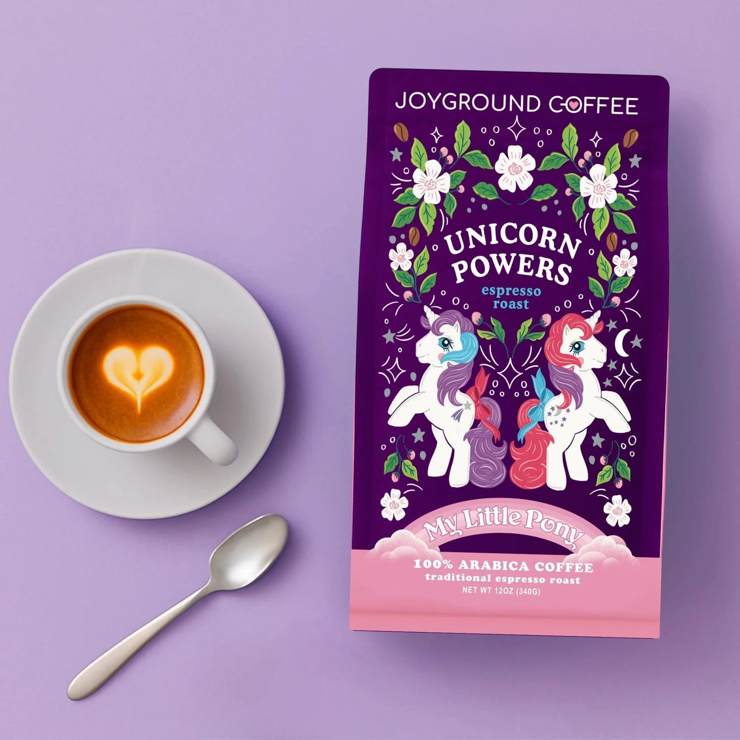 Unicorn Powers Joyground Coffee purple and pink coffee bag on a lavender surface next to an espresso mug, saucer, and spoon.