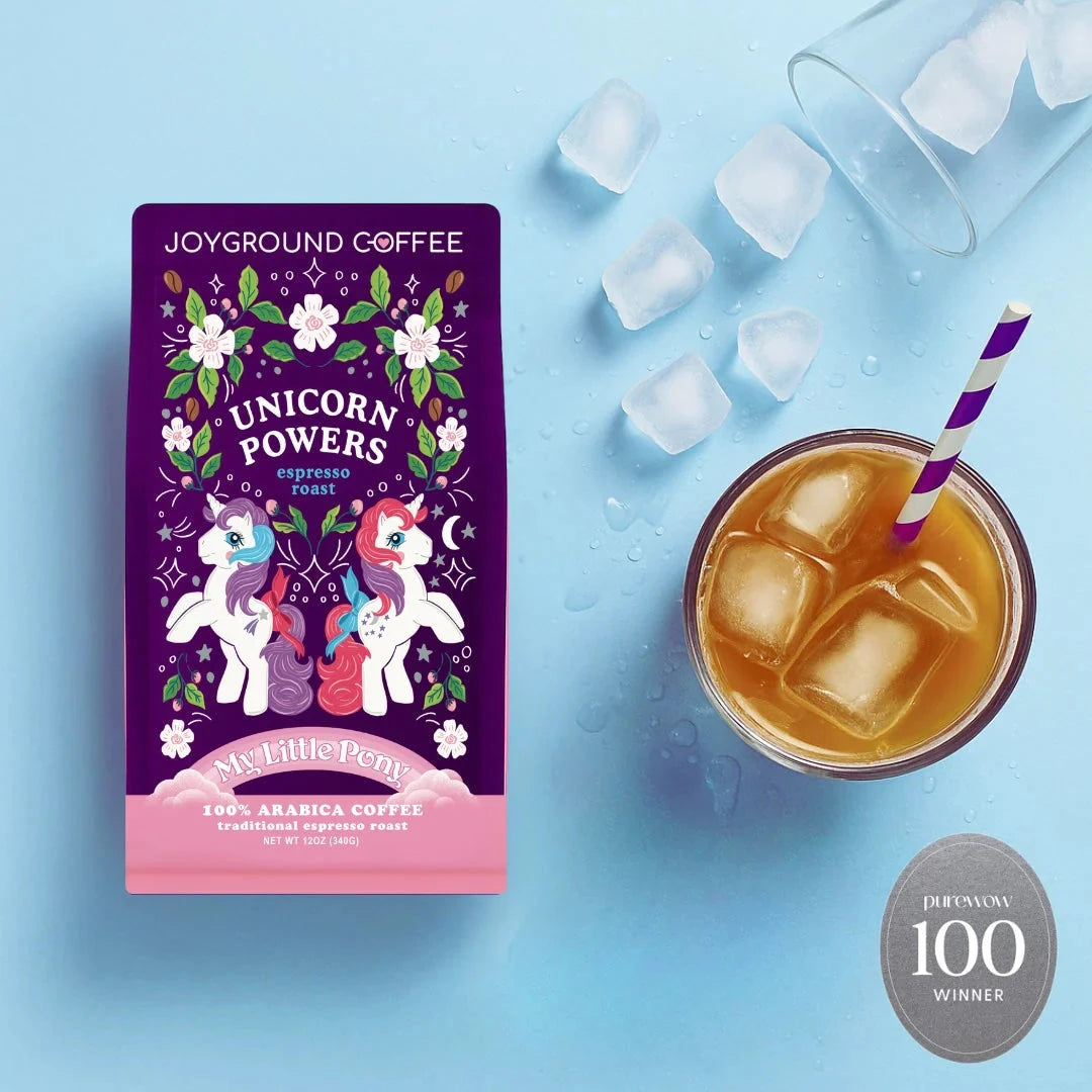 Unicorn Powers Joyground Coffee bag next to a glass of iced coffee with a purple striped straw, along with a badge indicating it was a PureWow winner for best Coffee for Cold Brew.